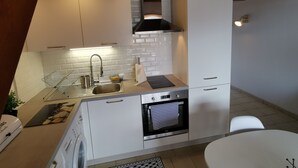 A compact kitchen with white cabinets, a stainless steel sink, a built-in oven, and a hanging pot rack.