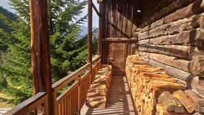 Una terraza de madera con barandilla, rodeada de troncos apilados, con vistas a un área boscosa.