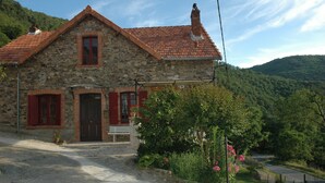 Ein Steinhaus mit rotem Ziegeldach, einer Holztür und einer Bank davor.