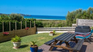 Un patio con tavolo e sedie in legno, vista sull'oceano e una recinzione di legno con piante in vaso.