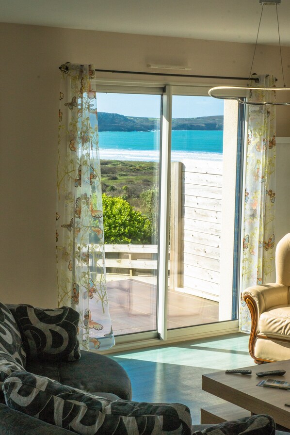 A living room with a sofa, a coffee table, and a view of the sea through a sliding glass door.