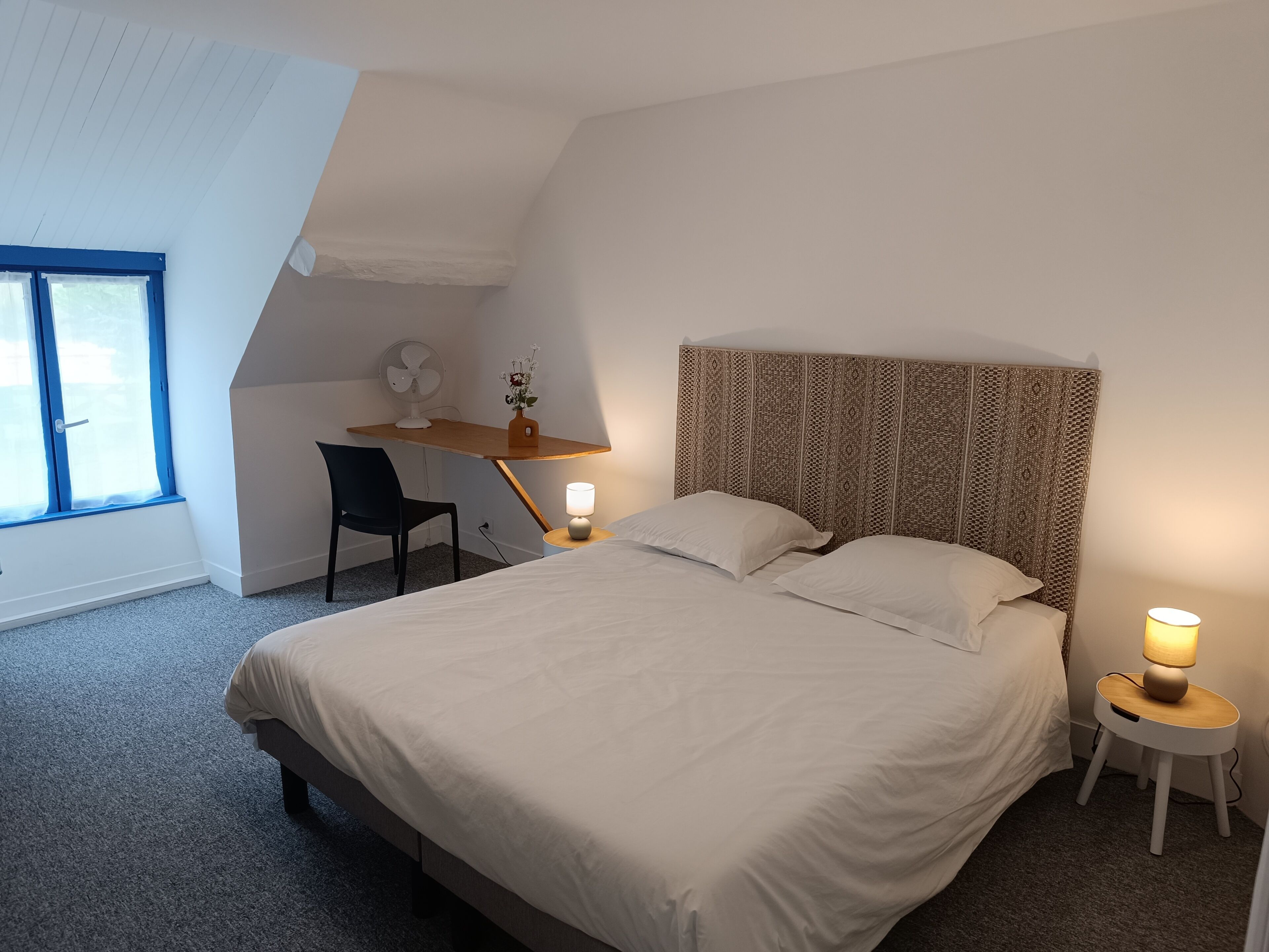 Une chambre à coucher avec un lit, un bureau, une chaise, une lampe et une fenêtre.