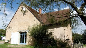 A rustic stone building with a sloped roof, a wooden door, and a small garden area with a wooden fence. - Rental bed and breakfast and gite in Lignieres 18160 (Lignières)