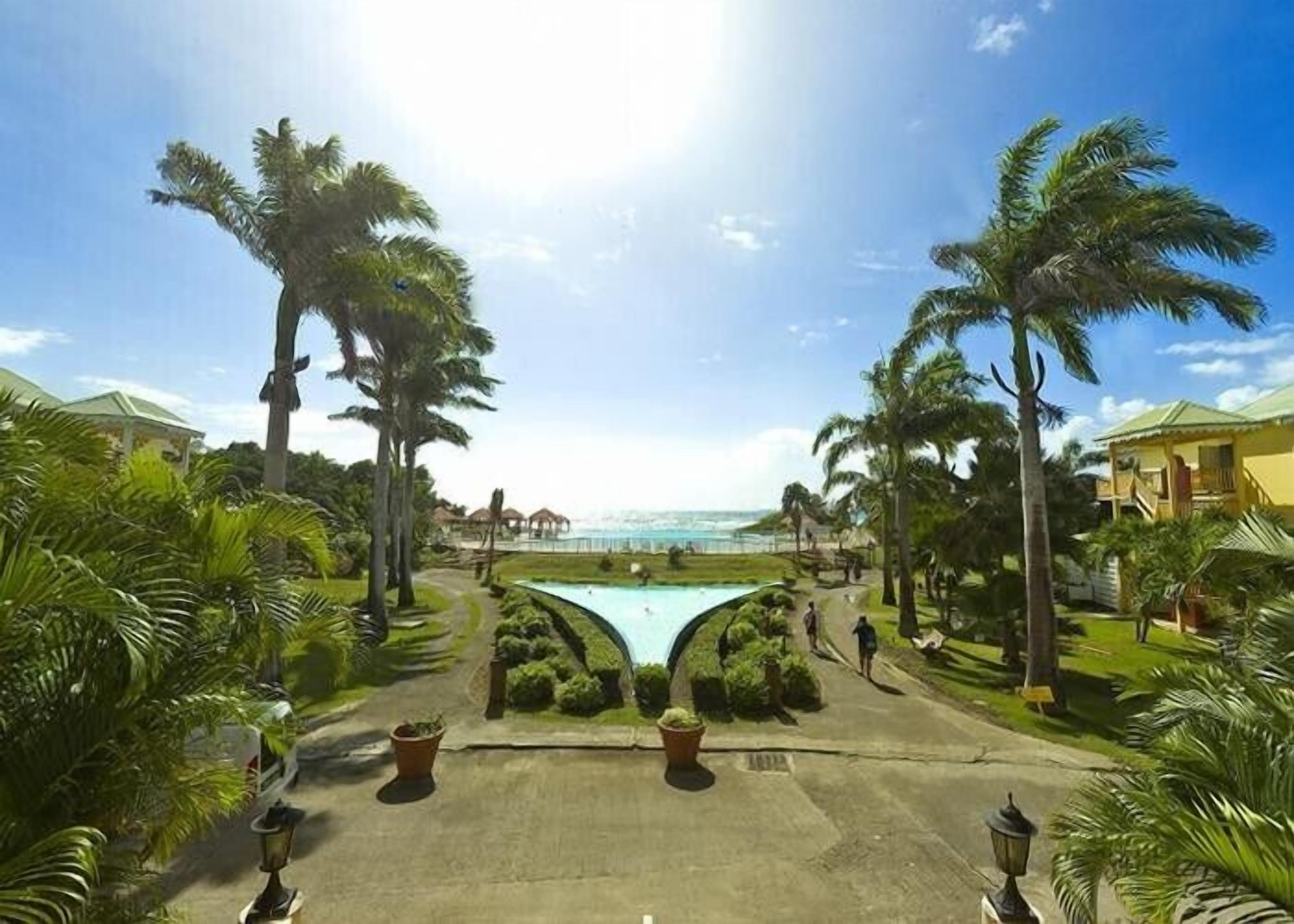 Un resort con piscina centrale, palme e vista sull'oceano.
