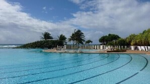 A large, clear swimming pool with multiple lanes, surrounded by palm trees and a view of the ocean. - Promotions 280th week Beautiful apartment StFrançois Domaine Anse des Rocher (97180)