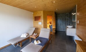 A spa room with two sunbeds, a small table with a book and a bowl of fruit, and a separate bathroom with a sink and shower. - La Marcairie Grand Chalet - Spa Luxury 5 stars (Muhlbach-Sur-Munster)