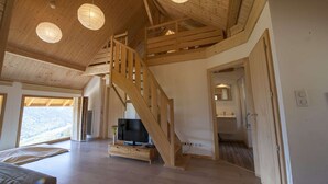 A spacious living area with a wooden staircase, a flat-screen TV on a wooden stand, and a view of the outdoors. - La Marcairie Grand Chalet - Spa Luxury 5 stars (Muhlbach-Sur-Munster)