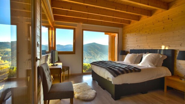 A bedroom with a bed, a desk, and a chair, with large windows offering a mountain view. - La Marcairie Grand Chalet - Spa Luxury 5 stars (Muhlbach-Sur-Munster)