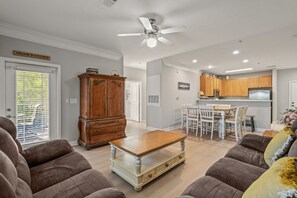 Uma sala de estar com um armário de madeira, uma mesa de jantar com cadeiras, uma área de cozinha com armários de madeira e um ventilador de teto.