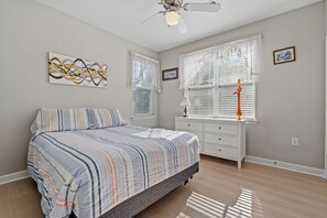 Um quarto com cama, cômoda, ventilador de teto e janela com persianas.