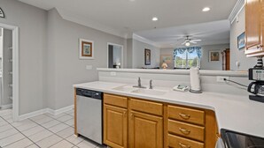 A modern kitchen with a dishwasher, double sink, wooden cabinets, and a large mirror. - 1115 Crow Creek Drive (Calabash)