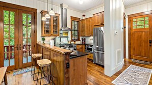 A kitchen with wooden cabinets, a central island, bar stools, and a view through the glass doors. - Owl's Nest - 2/2.5, Luxurious, Pet Friendly Home (Black Mountain)