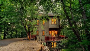 A two-story stone building with multiple windows, a wooden deck, and a gravel driveway. - Owl's Nest - 2/2.5, Luxurious, Pet Friendly Home (Black Mountain)