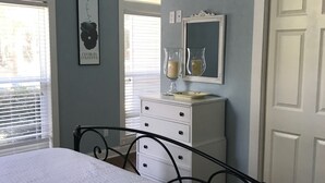 A bedroom with a bed, a dresser, a mirror, and a window with blinds.