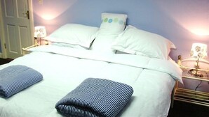 A neatly made bed with white linens and striped pillows, two bedside lamps, and a door in the background.