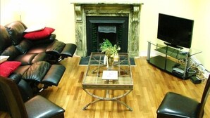 A living room with a leather sofa, a glass coffee table, a fireplace, and a television.