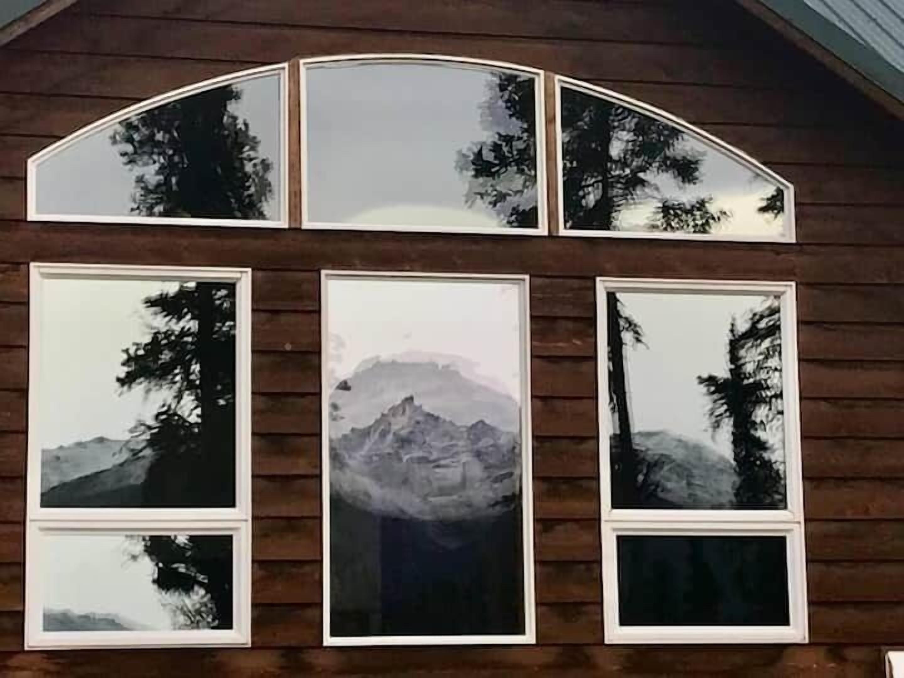 A wooden cabin with a large arched window and multiple framed pictures of mountains and trees.