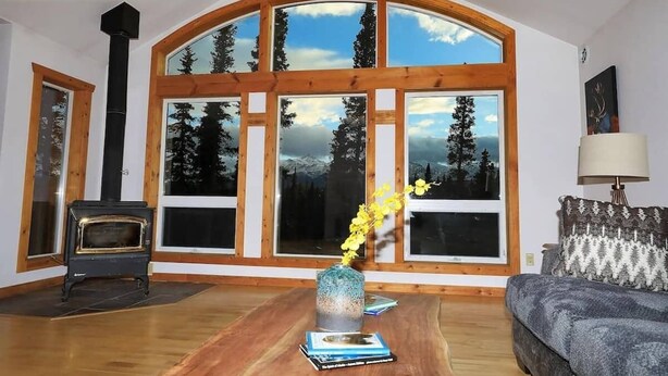 A living room with a large arched window, a wood-burning stove, a sofa, and a vase with flowers. - 3 Bedroom Home with Amazing Views 11 mi from Denal (Healy)