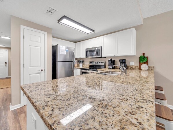 A modern kitchen with white cabinets, stainless steel appliances, granite countertops, and a built-in microwave.