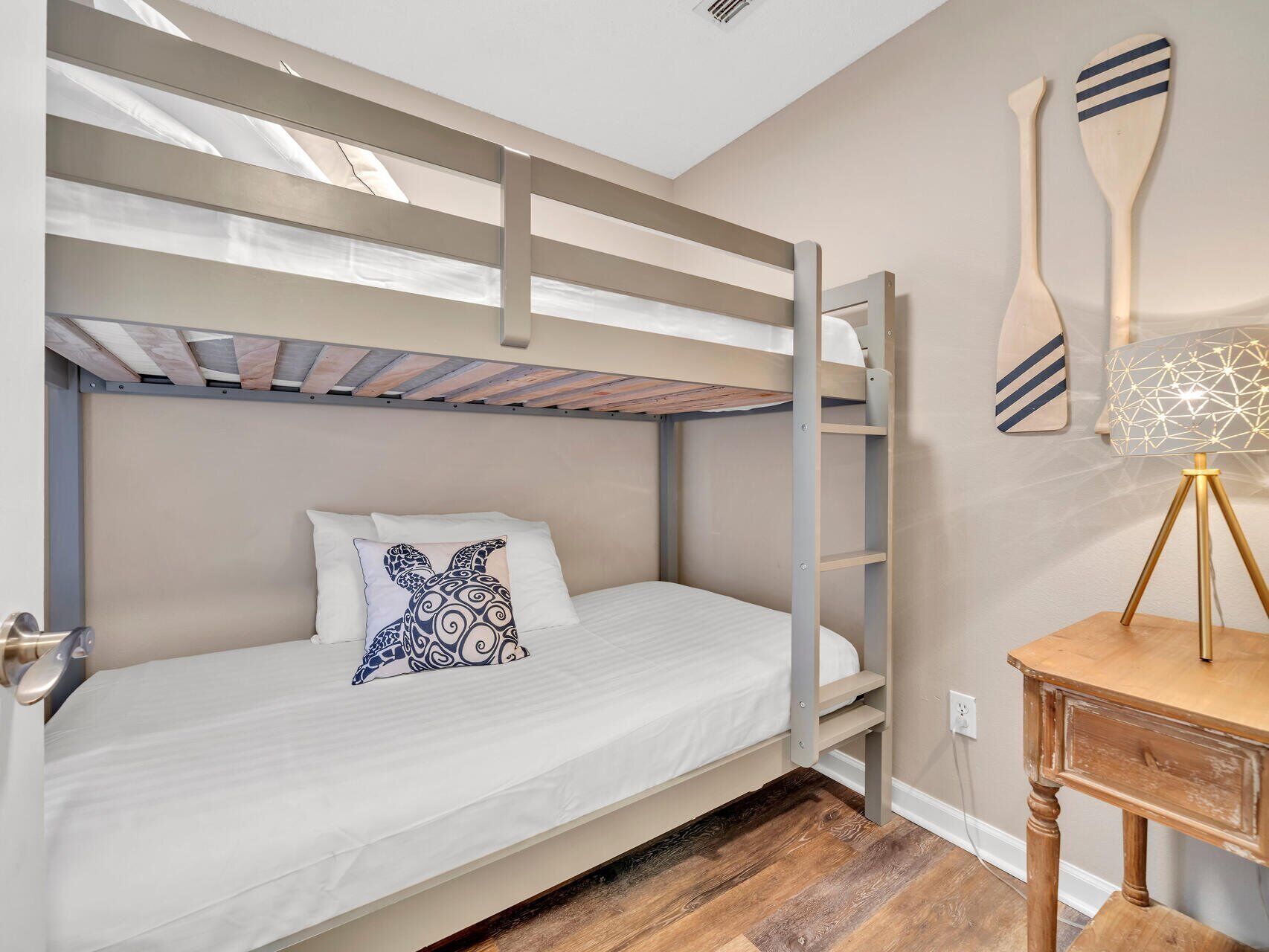 A bunk bed room with a white mattress, a patterned pillow, and a wooden floor.
