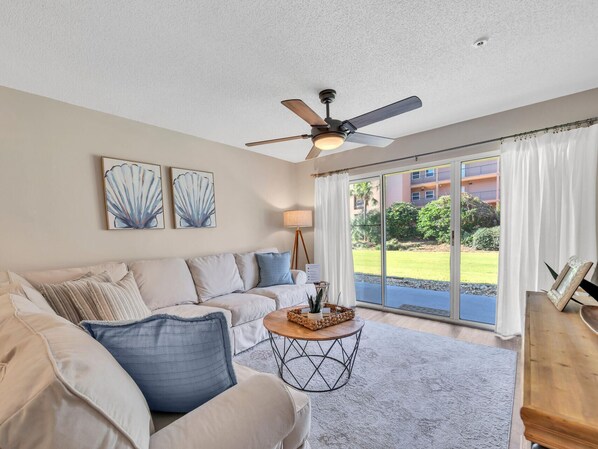 A spacious living room with a beige sofa, a round coffee table, and a ceiling fan. - Free Amenities, Gulf-view! Private Beach! Pool! Ciboney 1009! (Destin)