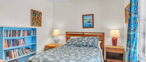 A bedroom with a bed, a bookshelf, two bedside tables with lamps, and a window with curtains.