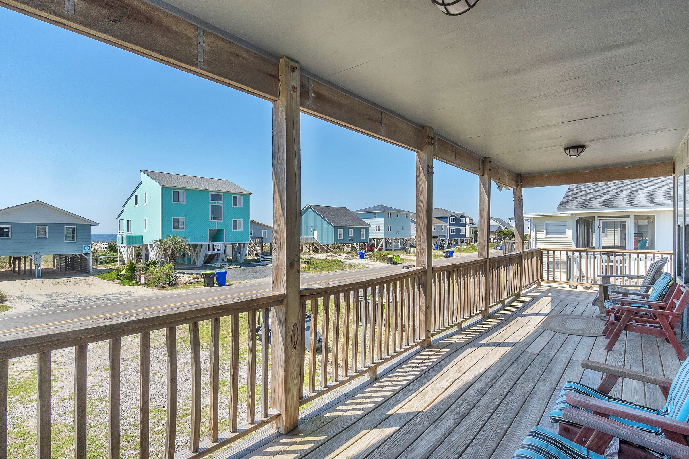 Une terrasse en bois dotée d’une rambarde, qui offre une vue sur une plage bordée de maisons.