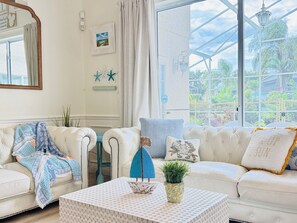 Una habitación bien iluminada con un sofá blanco, un plaid estampado y un pequeño modelo de velero sobre una mesa.