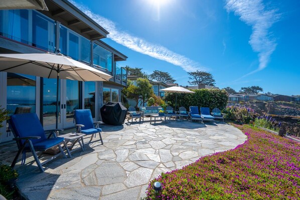 Une terrasse avec un sol en pierre, du mobilier d’extérieur et une vue sur l’océan.