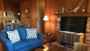 Ein gemütliches Wohnzimmer mit einem blauen Sofa, einem Couchtisch, einem Fernseher und einem Kamin.