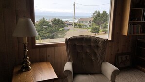 Ein Zimmer mit Meerblick, ein Sessel, ein Tisch mit Lampe und ein Bücherregal.