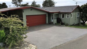 Ein eingeschossiges Haus mit roter Garagentür, einer Auffahrt und einem Kiesrand entlang der Auffahrt.