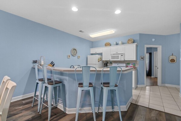 A kitchen with a central island, white cabinets, and blue chairs.
