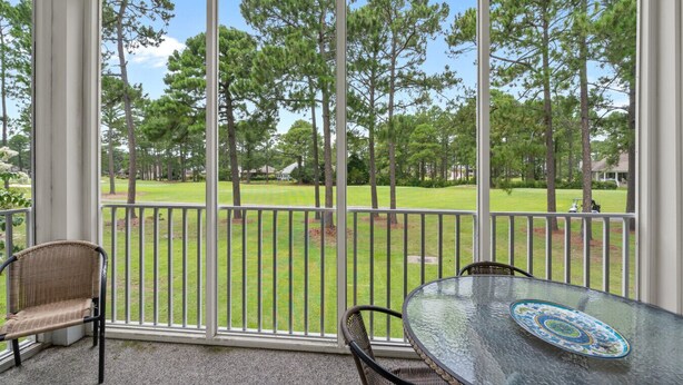 A covered patio with a glass table and wicker chairs, overlooking a well-maintained lawn and trees. - 3709 Champions at Sea Trail (Sunset Beach)