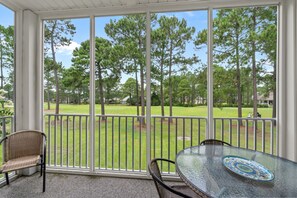 A covered patio with a glass table and wicker chairs, overlooking a well-maintained lawn and trees.