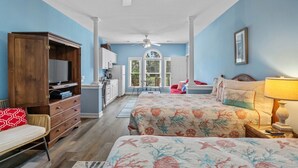 A bedroom with a large bed, a desk, a chair, a wardrobe, and a kitchenette. - 3709 Champions at Sea Trail (Sunset Beach)