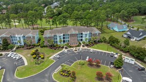 An aerial view of a hotel with multiple buildings, a parking lot, and surrounding greenery. - 3709 Champions at Sea Trail (Sunset Beach)