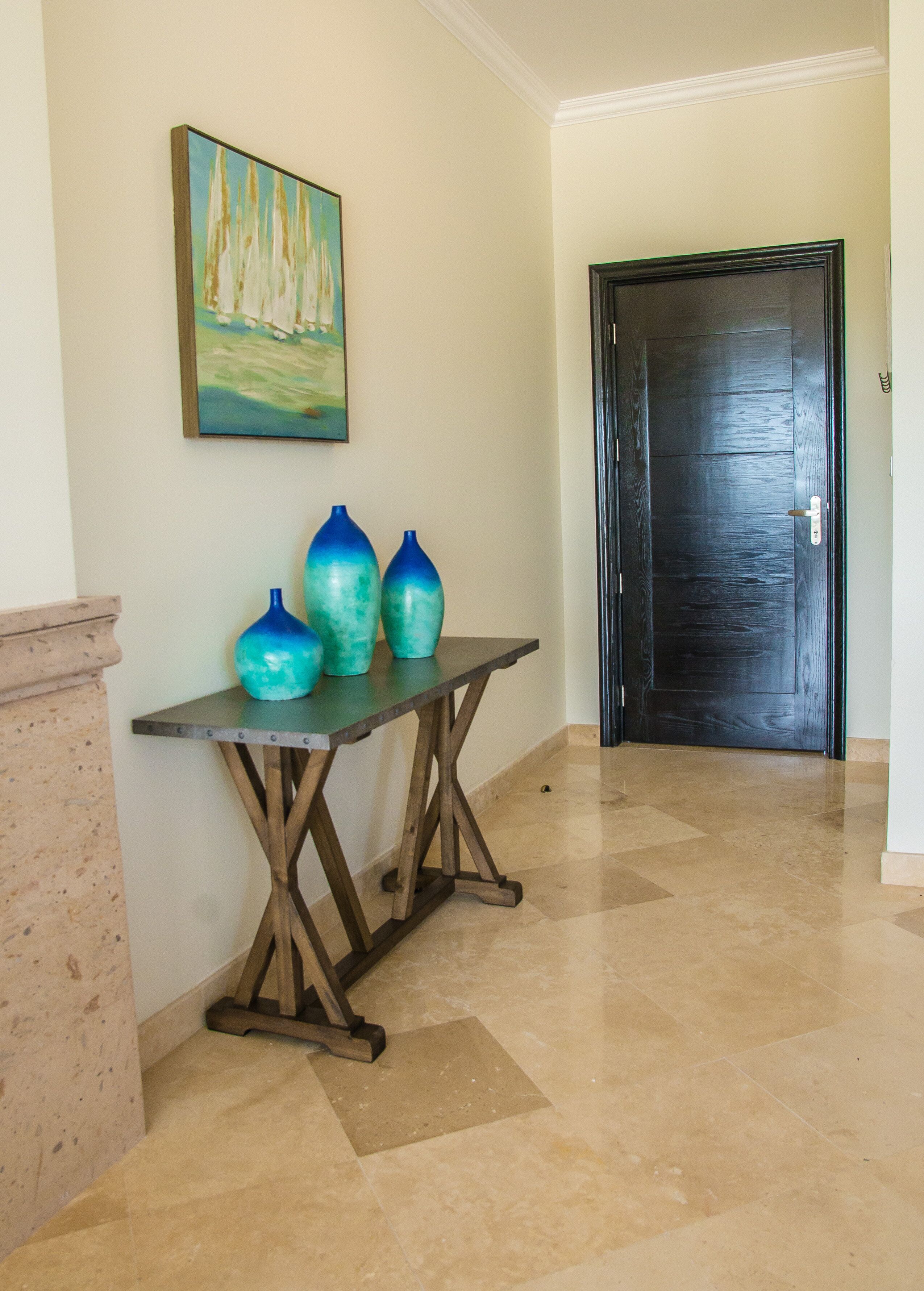 A hallway with a tiled floor, a dark wooden door, and a table with two blue vases.