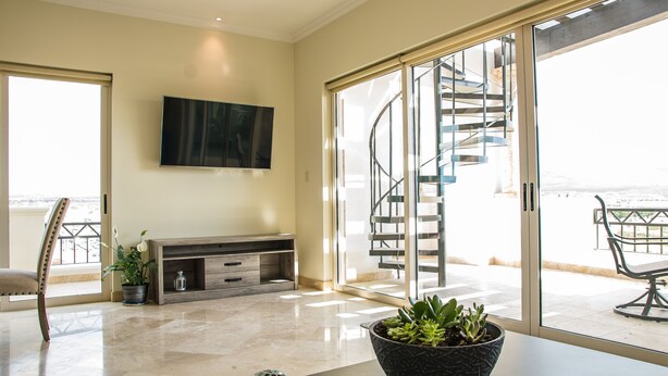 Un vaste espace de vie doté d’une grande fenêtre, d’un téléviseur à écran plat, d’un escalier menant à un espace extérieur et d’une table à manger agrémentée d’objets décoratifs.