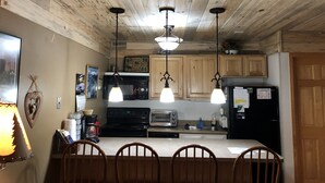 Une cuisine avec des meubles de rangement en bois, un réfrigérateur noir, une cuisinière, un grille-pain et des luminaires suspendus.