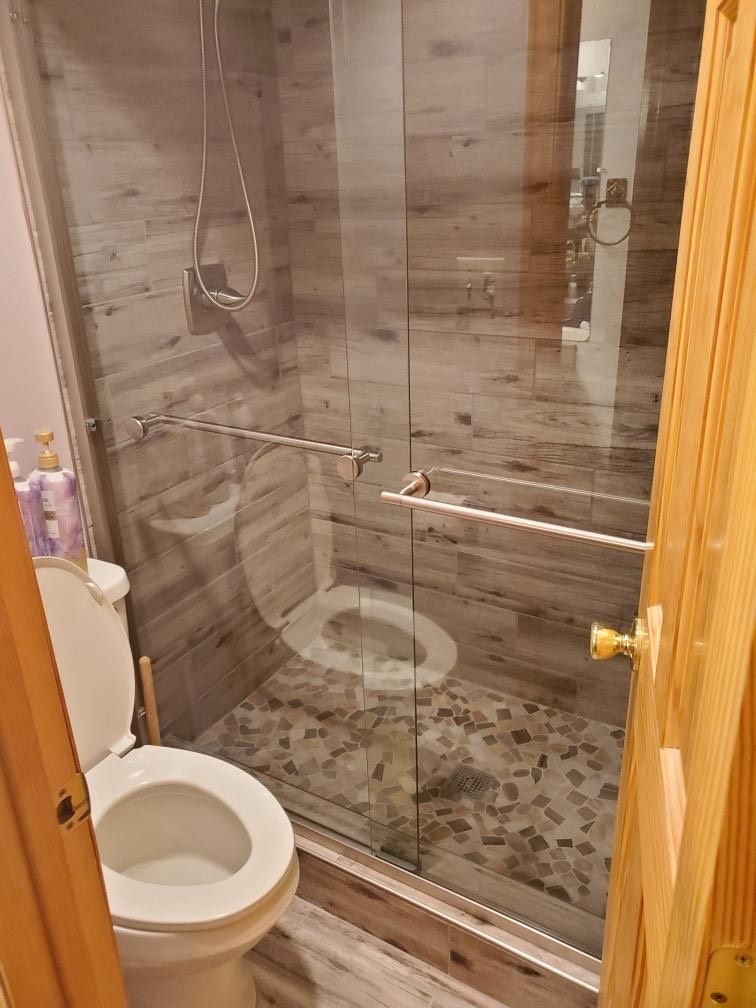 A bathroom with a glass-enclosed shower, a toilet, and a tiled floor.