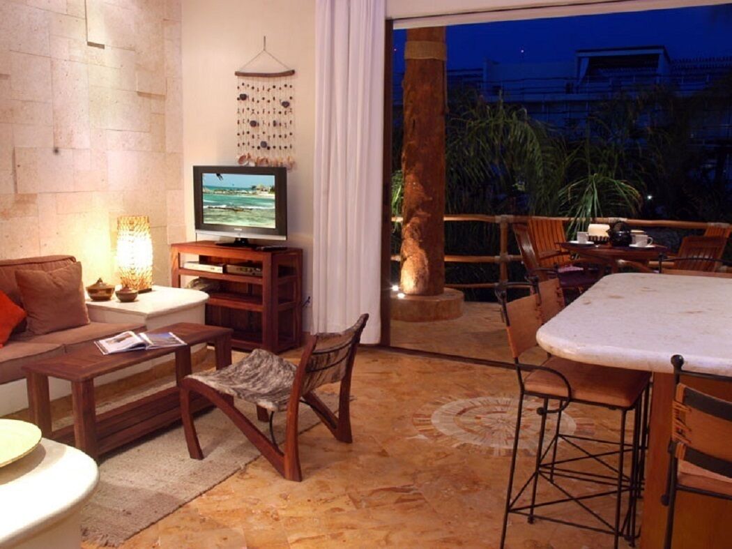 A living room with a television, sofa, coffee table, and chairs. There is a balcony with a table and chairs.