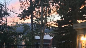 A hot tub with a wooden deck, a metal fence, and a view of a residential area with trees and a house in the background. - Buttes Condo, Steps from the base area, Mountain Luxury (Crested Butte)
