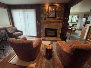 A cozy living room with a stone fireplace, comfortable seating, and a dining area visible in the background. - Buttes Condo, Steps from the base area, Mountain Luxury (Crested Butte)