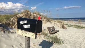 En brevlåda med texten ”KNORED SPIRIT” står på en sandstrand, fastsatt på en trästolpe, och en röd flagga vajar.