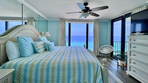 Un dormitorio con una cama grande, ventilador de techo, televisor, cómoda y vista al océano.