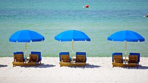 Tres sillas de playa con sombrillas azules en una playa arenosa.