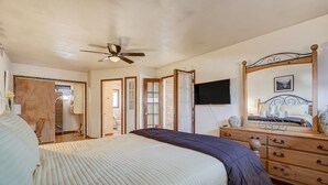A bedroom with a bed, a dresser, a mirror, a ceiling fan, and a TV.
