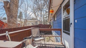 A wooden deck with a chair and a table, a blue building, and a tree.