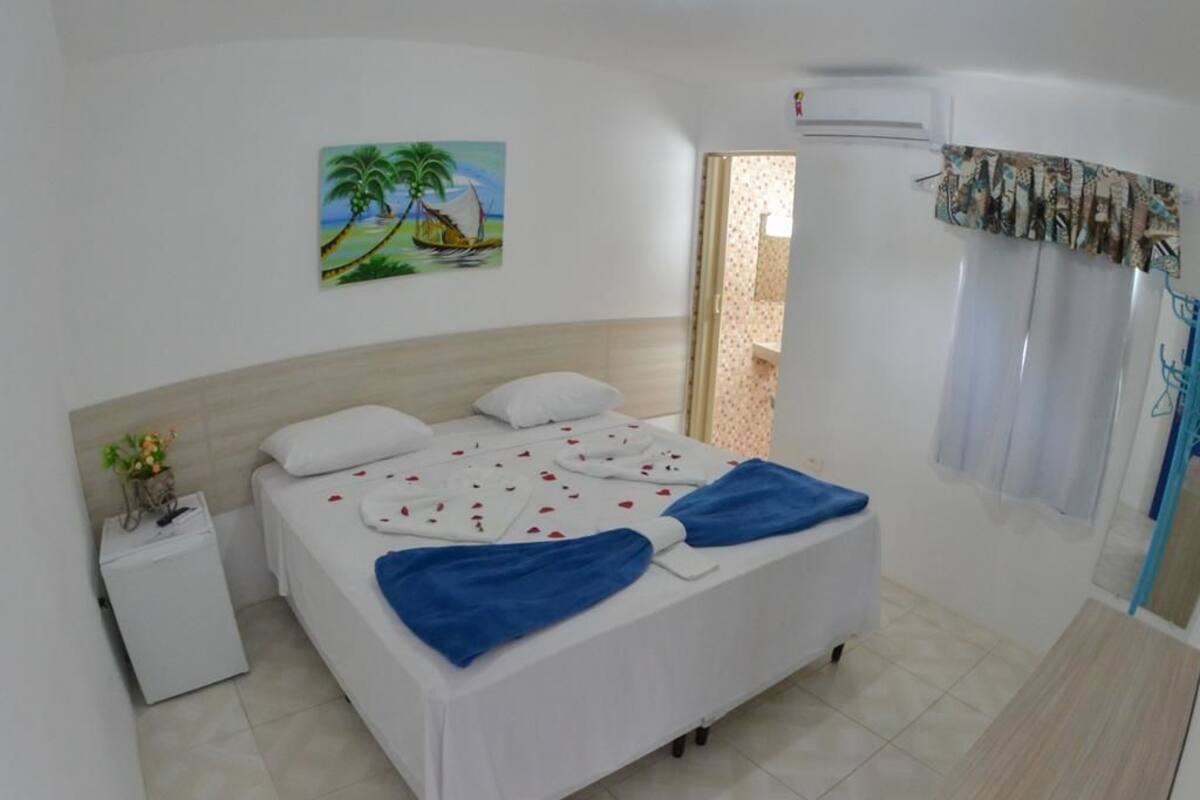 A bedroom with a bed, a nightstand, a painting, and a window with curtains.